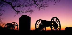 Silhouette of historical cannons at sunset with vibrant purple and orange sky and bare tree branches