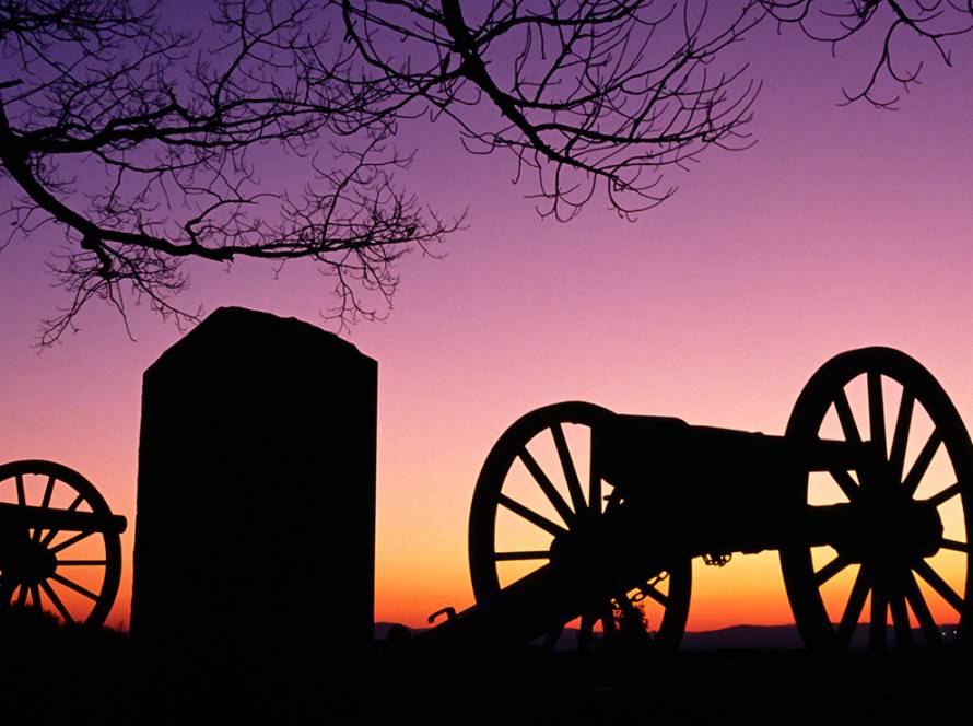 Silhouette of historical cannons at sunset with vibrant purple and orange sky and bare tree branches