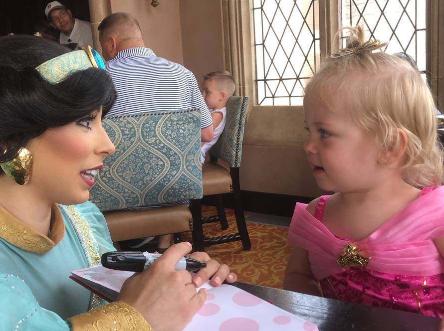 Princess character interaction with young girl in a pink dress at a themed restaurant