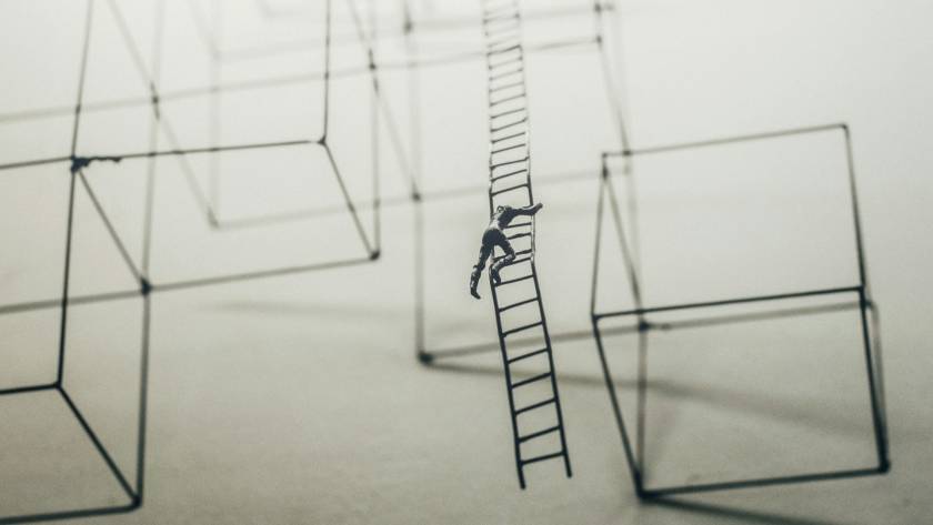 Miniature figure climbs ladder among geometric wireframe structures in abstract setting
