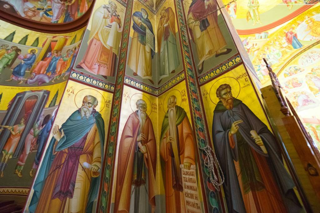 Colorful Orthodox church interior with detailed religious iconography on decorated walls and ceiling depicting saints