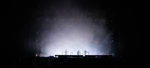 Silhouettes of performers on a dark, misty stage with dramatic lighting effects at a live concert event