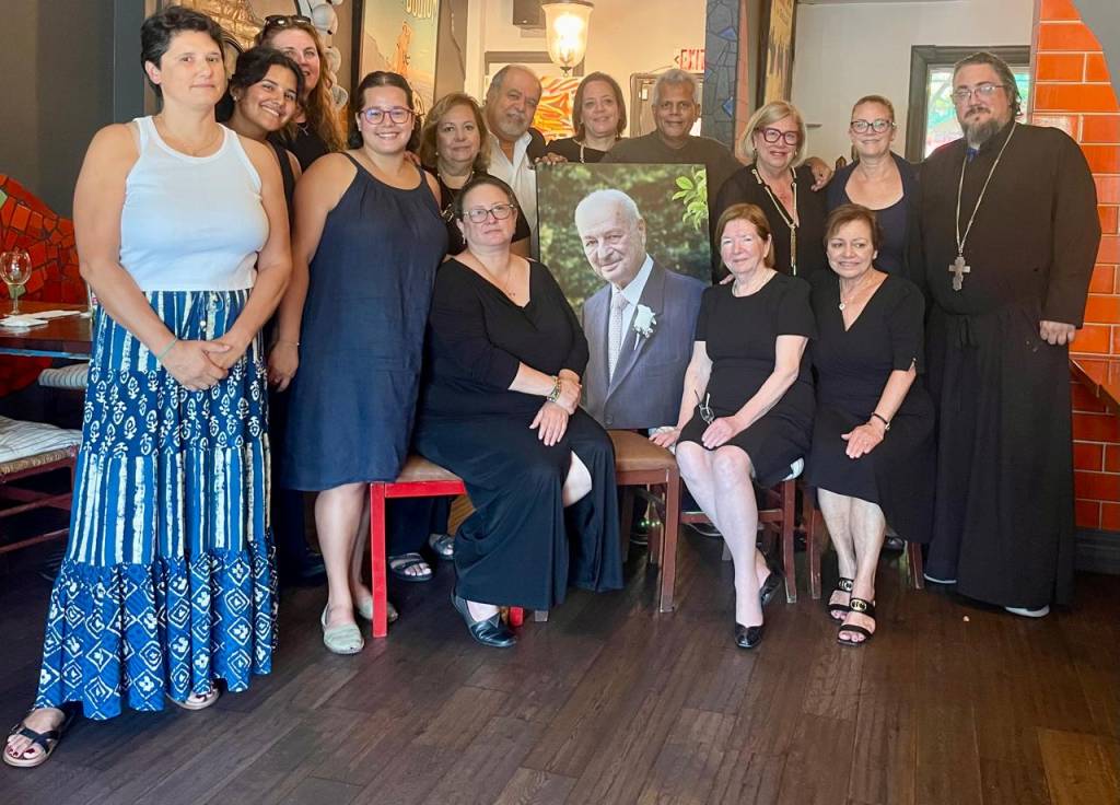 Group gathered around a framed portrait at a commemorative event indoors