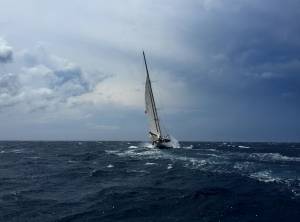 Sailboat navigating rough ocean waters under cloudy skies, capturing adventure and the power of nature