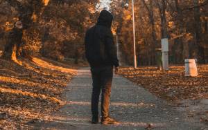 Person in a hoodie walking on a leaf-covered path during autumn in a forest setting
