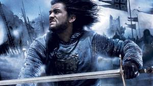 Medieval warrior with sword and chainmail armor in intense battle scene with flags and castle background