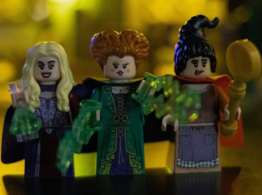 Three witch-themed LEGO minifigures with glowing backgrounds holding green potion elements and a broomstick
