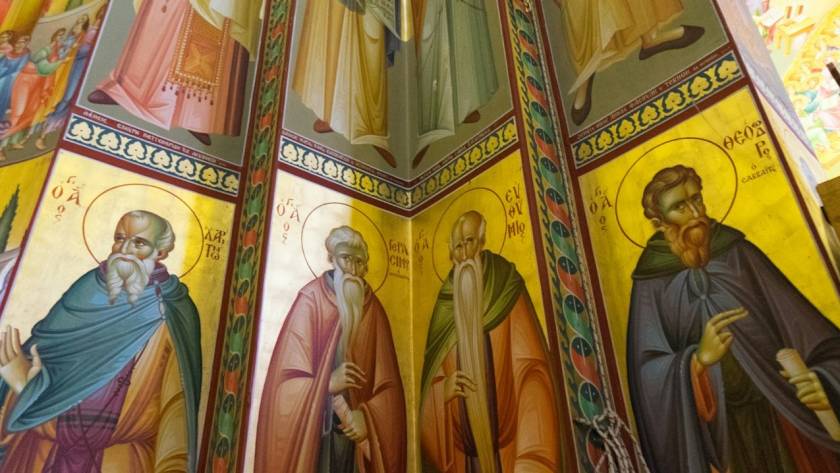 Colorful religious murals depicting saints adorn a church's interior walls, highlighting intricate iconography