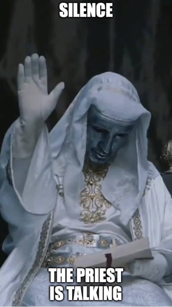 Masked figure dressed as a priest raising hand while reading, with Silence, the priest is talking text overlay