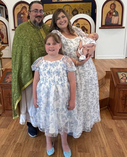 Family dressed in white and green stands inside a church, with icons in the background