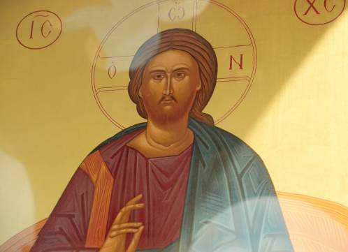 Icon of religious figure with halo and hand raised in blessing gesture, traditional art style with vivid colors